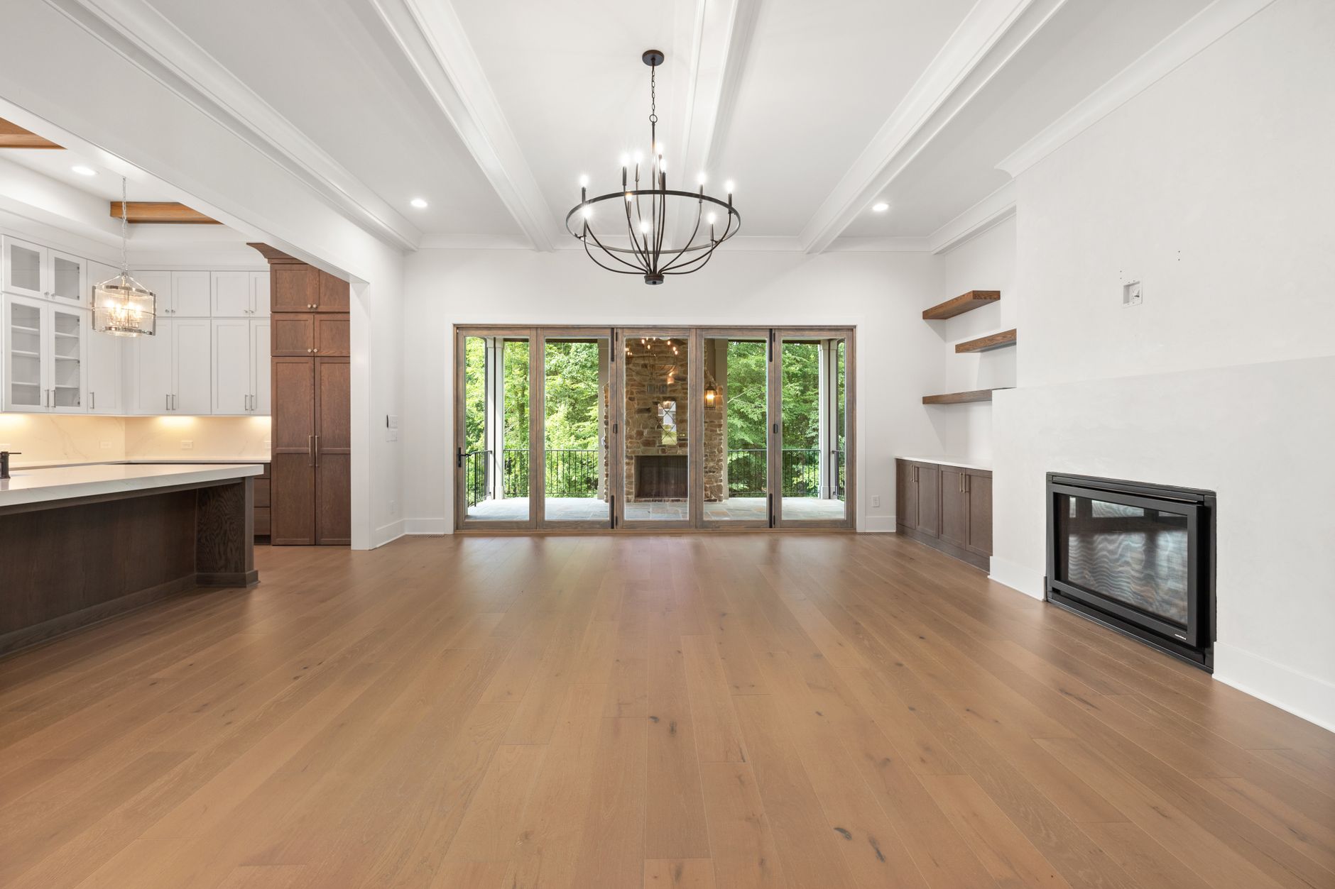 Wide-plank hardwood flooring running through an open Arkansas living room and on into the kitchen, with a fireplace and garden doors