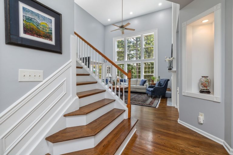 Oak stair treads on white risers in an Arkansas foyer, open on one side to a living room with a hardwood floor