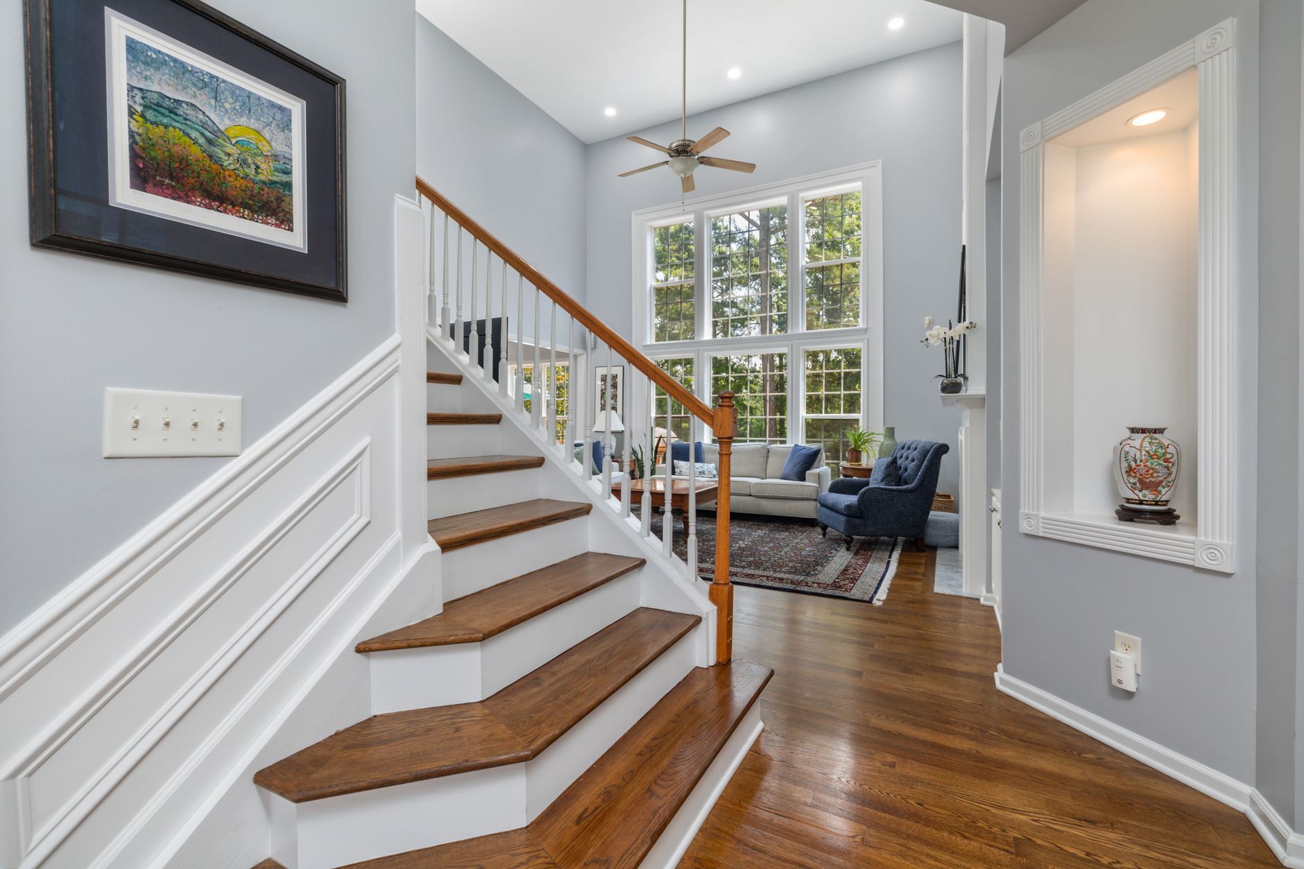 Oak stair treads on white risers in an Arkansas foyer, open on one side to a living room with a hardwood floor