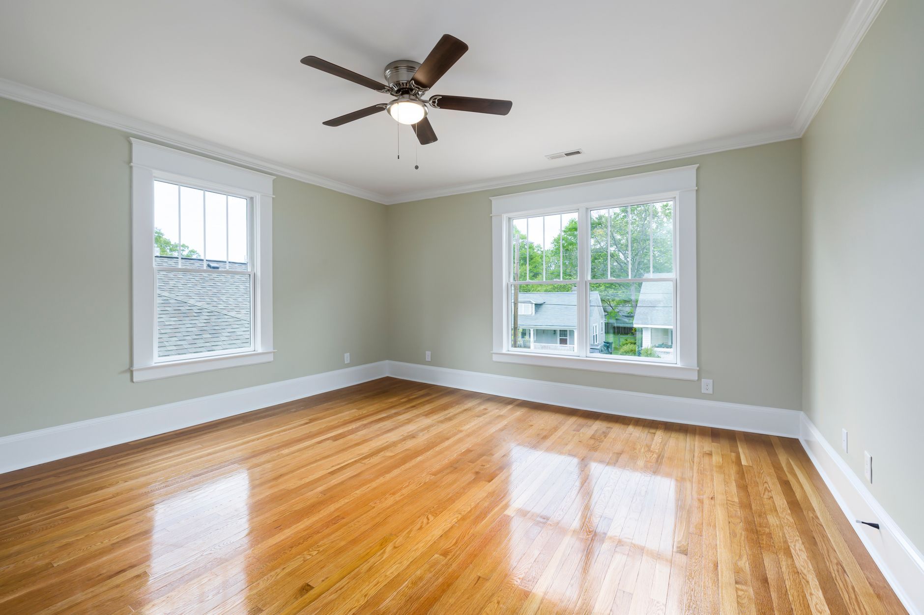 Bright empty room with wooden floors, large windows, and a ceiling fan