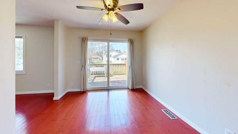 Spacious empty room with red wooden flooring, ceiling fan, and patio view